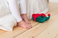 Horizontal shot of unrecognizable little small child stands on wooden floor with elf s shoes, sits on white bedclothes Royalty Free Stock Photo