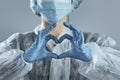 Woman in medical mask and hands in latex glove shows the symbol of the heart