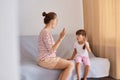 Horizontal shot of woman speech pathologist having lesson with little girl, people sitting on comfortable sofa near window,