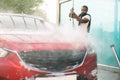 Horizontal shot of young African American man washing his luxury red car under high pressure water jet outdoors at self Royalty Free Stock Photo