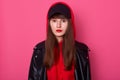 Horizontal shot of young beautiful fashionable teenager girl wearing leather jacket, red hoody and black cap, looking directly at Royalty Free Stock Photo