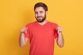 Horizontal shot of young beraded male, looking directly at camera, wearing casual bright red t shirt, standsing against white