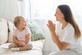 Smiling mother clapping and looking at happy toddler sitting on couch in living room Royalty Free Stock Photo