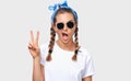 Horizontal studio portrait of cheerful blonde young woman wearing trendy sunglasses, white t-shirt and blue headband, showing Royalty Free Stock Photo