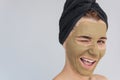 Horizontal studio portrait of happy young woman blink with eye with cosmetic green clay organic mask on her face, wears black Royalty Free Stock Photo