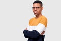 Horizontal studio portrait of pleasant African American young man wearing trendy sweater keeps crossed hands, looking to the Royalty Free Stock Photo