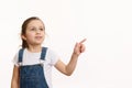 Horizontal shot of a happy little girl in blue denim overalls, pointing away on free space for your advertising content Royalty Free Stock Photo