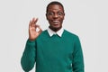 Horizontal view of attractive young black man with toothy smile, shows okay gesture, says alright, likes somebodys idea Royalty Free Stock Photo