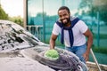 Horizontal view of car cleaning at self wash service outdoors. Handsome African man in casual wear looking at camera