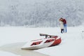 Horizontal view of the cheerful beautiful couple standing in the front of the snowy boat. The man is kissing his red