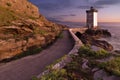 Horizontal view of a path, rocks and a small lighthouse next to a seaside under a blue sky Royalty Free Stock Photo