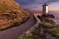 Horizontal view of a path, rocks and a small lighthouse next to a seaside under a blue sky