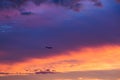 Horizontal view of plane flying above sunset with dramatic coloured sky