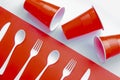 Horizontal view of single use white plastic cutlery and red plastic glass on a red and white background. Concept: Ban single use Royalty Free Stock Photo