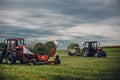 Horizontal view of tractors harvesting grass under cloudy sky