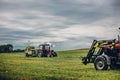 Horizontal view of tractors harvesting grass under cloudy sky Royalty Free Stock Photo