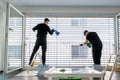 Two male professional cleaners cleaning blinds on a large window front with micro fiber cloths