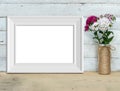 Horizontal A4 Vintage White Wooden Frame mockup near a bouquet of sweet-william stands on a wooden table on a painted white
