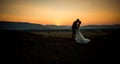 Horizontal wedding shot of the charming newlywed couple kissing at the edge of the mountains during the sunset. Royalty Free Stock Photo