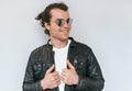 Horizotal studio portrait of handsome male model with curly hair wears mirror glasses and leather jacket, smiling and looking away Royalty Free Stock Photo