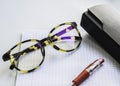 Horn-rimmed glasses, red ink pen and glasses case on a checkered notebook