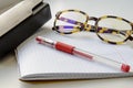 Horn-rimmed glasses, red ink pen and glasses case on a checkered notebook