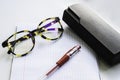 Horn-rimmed glasses, red ink pen and glasses case on a checkered notebook