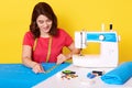 Horozontal shot of smiling young woman sewing with professional machine at workshop, taking measurment and using signing chalk,