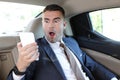 Horrified businessman stressed out in backseat holding mobile phone