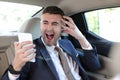 Horrified businessman stressed out in backseat holding mobile phone