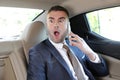 Horrified businessman stressed out in backseat holding mobile phone