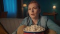 Horror film. Shocked young woman watching a scary movie on TV at home and eating popcorn. The woman shudders and spills