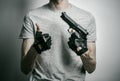 Horror and firearms topic: the killer with a gun in his hand in black gloves on a gray background in the studio Royalty Free Stock Photo