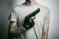 Horror and firearms topic: the killer with a gun in his hand in black gloves on a gray background in the studio Royalty Free Stock Photo