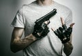 Horror and firearms topic: the killer with a gun in his hand in black gloves on a gray background in the studio Royalty Free Stock Photo