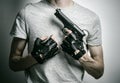 Horror and firearms topic: the killer with a gun in his hand in black gloves on a gray background in the studio Royalty Free Stock Photo