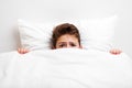 Scared peeking child boy lying bed covering face with blanket