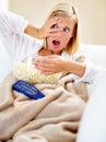 Horror, popcorn and woman on couch watching tv with remote, blanket and streaming movies in home. Terror, television and