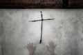 A horror spooky concept. A wooden cross made out of twigs, hanging on a white wall, with two ghostly, transparent hands coming up