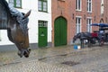 Horse-drawn carriage with tourists and Drinking fountain for horses in historic center of Bruges, Belgium, selective focus