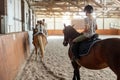 Horse riding school. Little children girls at group training equestrian lessons in indoor ranch horse riding hall. Cute Royalty Free Stock Photo