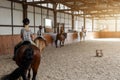 Horse riding school. Little children girls at group training equestrian lessons in indoor ranch horse riding hall. Cute Royalty Free Stock Photo