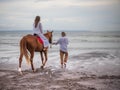 Horse riding by the sea. Woman on a brown horse. Man leading horse by its reins. Love to animals. Husband and wife spending time Royalty Free Stock Photo