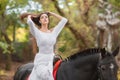 Horseback riding. Beautiful young woman in a white dress riding on a brown horse outdoors. Royalty Free Stock Photo