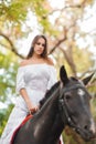 Horseback riding. Beautiful young woman in a white dress riding on a brown horse outdoors. Royalty Free Stock Photo