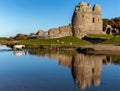 Horses crossing a river next to the ruins of an ancient castle. Ogmore Castle,Wales