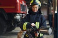 Hose in hands. Female firefighter in protective uniform standing near truck