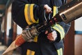 Hose in hands. Female firefighter in protective uniform standing near truck