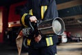 Hose in hands. Female firefighter in protective uniform standing near truck