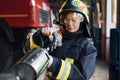 Hose in hands. Female firefighter in protective uniform standing near truck